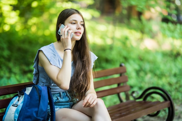 Feliz linda mujer joven caucásica sonríe y hablando por teléfono en el parque