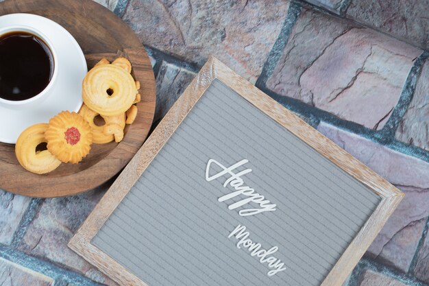 Feliz lunes en el tablero con una taza de bebida y galletas alrededor