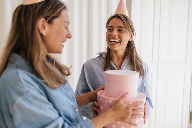 Feliz madre caucásica dando regalo de cumpleaños a una hija adolescente rubia aislada de fondo blanco. Concepto de vacaciones, celebración y mujeres.