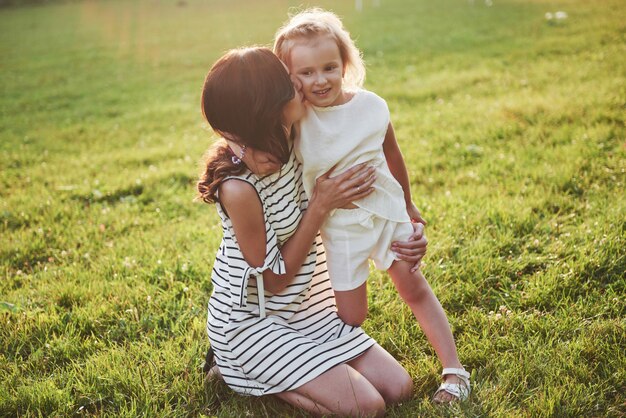 Feliz madre e hija abrazando en un parque en el sol en un brillante verano de hierbas.