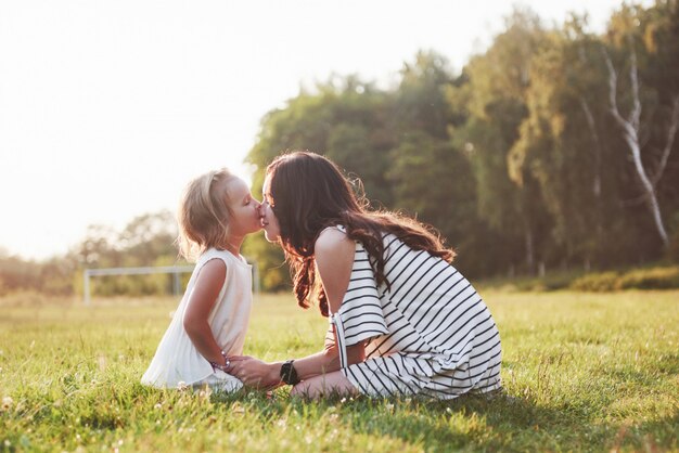 Feliz madre e hija abrazando en un parque en el sol en un brillante verano de hierbas.