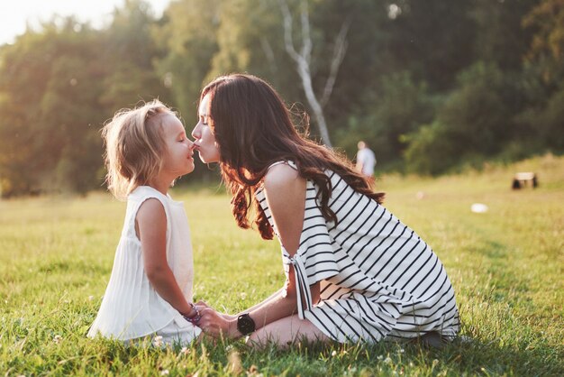 Feliz madre e hija abrazando en un parque en el sol en un brillante verano de hierbas.