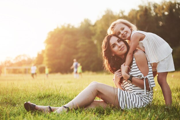 Feliz madre e hija abrazando en un parque en el sol en un brillante verano de hierbas.