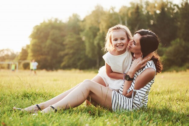 Feliz madre e hija abrazando en un parque en el sol en un brillante verano de hierbas.