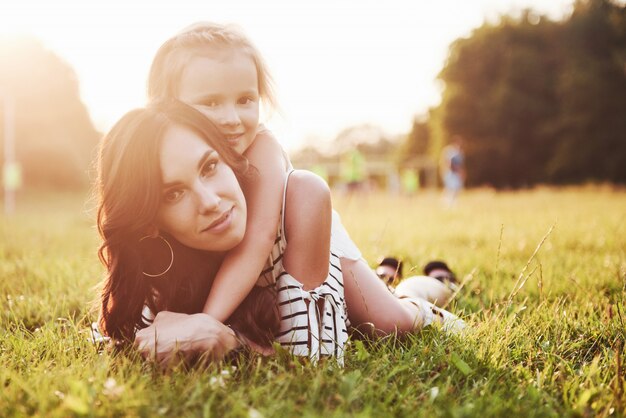 Feliz madre e hija abrazando en un parque en el sol en un brillante verano de hierbas.