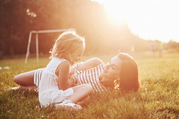 Feliz madre e hija abrazando en un parque en el sol en un brillante verano de hierbas.