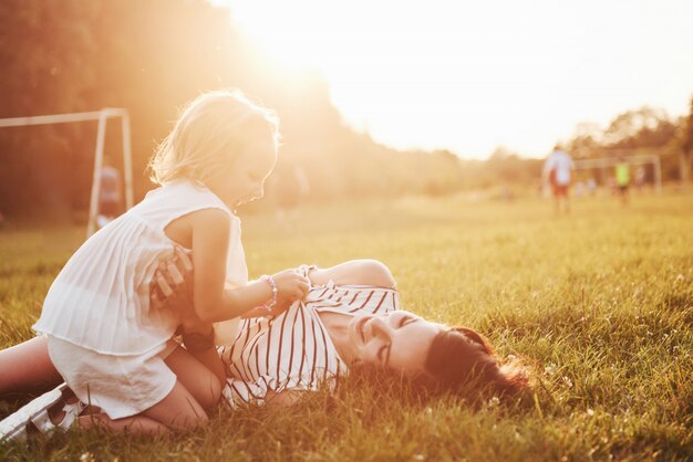 Feliz madre e hija abrazando en un parque en el sol en un brillante verano de hierbas.