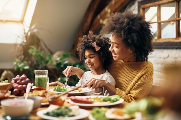 Feliz madre e hija afroamericana comiendo en la mesa de comedor