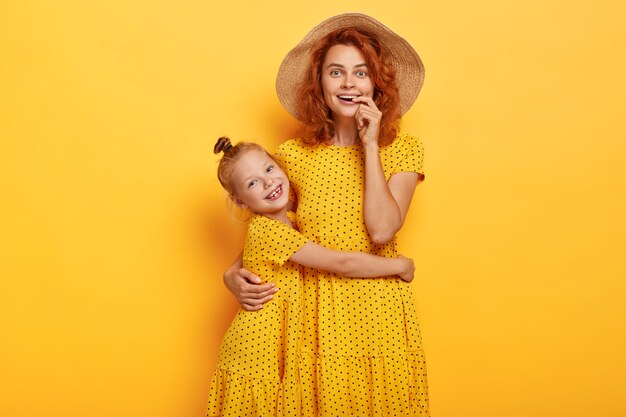 Feliz madre e hija pelirroja posando en vestidos similares