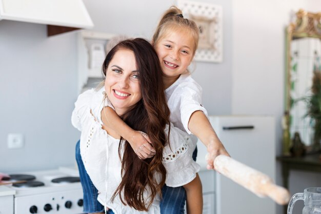 Feliz madre e hija posando con rodillo de cocina