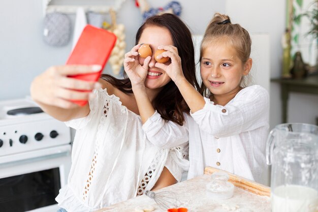 Feliz madre e hija tomando selfies con huevos