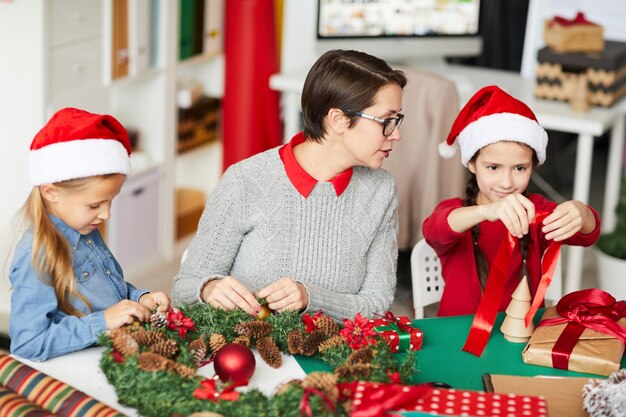 Feliz madre e hijas decorando la corona de navidad