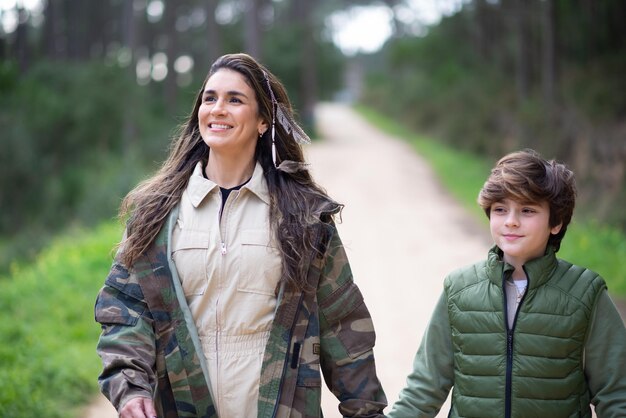 Feliz madre e hijo caminando en el bosque. Mujer y niño de pelo oscuro con abrigos caminando en un día nublado. Familia, naturaleza, concepto de ocio.