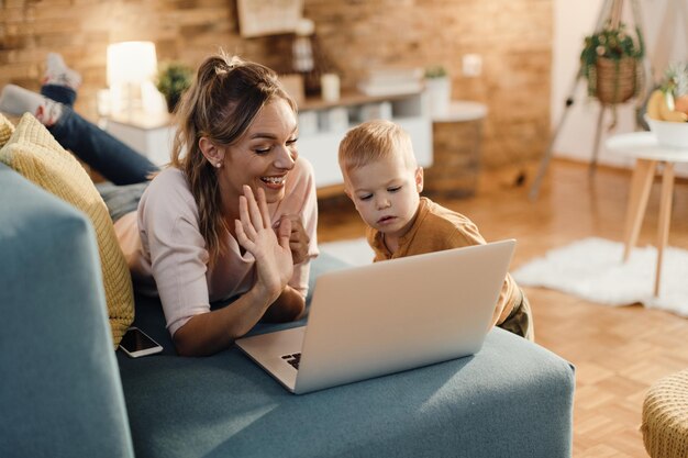 Feliz madre e hijo haciendo videollamadas a través de una laptop en casa