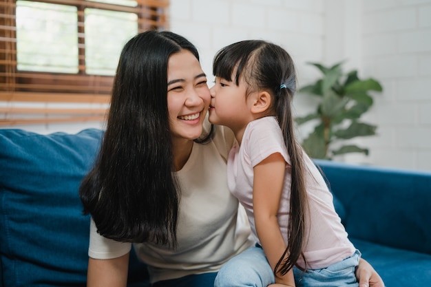 Feliz madre de familia asiática e hija abrazándose besándose en la mejilla felicitando con cumpleaños en casa.