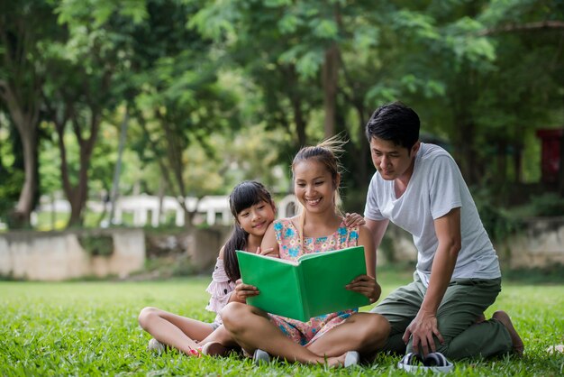 Feliz madre de familia, padre e hija leer un libro en el parque