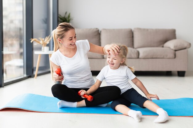 Feliz madre con hija en estera de yoga en casa