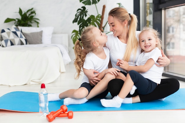 Feliz madre posando en casa en estera de yoga con hijas