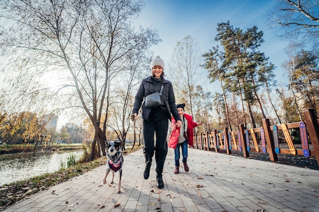Feliz madre y su hija caminan con perro en el parque otoño