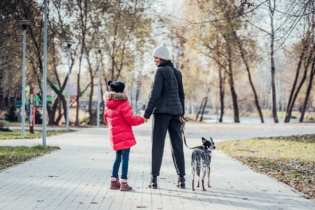 Feliz madre y su hija caminan con perro en el parque otoño