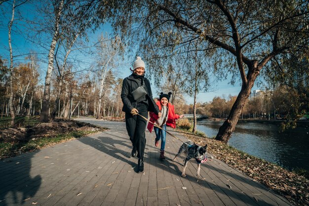 Feliz madre y su hija caminan con perro en el parque otoño