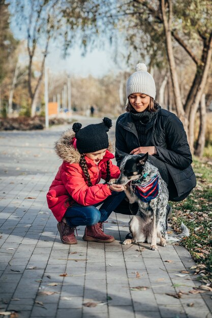 Feliz madre y su hija jugando con perro en el parque otoño