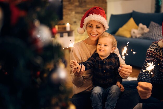 Feliz madre y su pequeño hijo divirtiéndose con bengalas en la víspera de Navidad