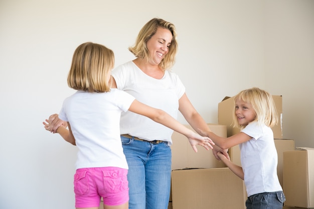 Feliz mamá rubia caucásica y dos chicas bailando en la habitación entre cajas de cartón