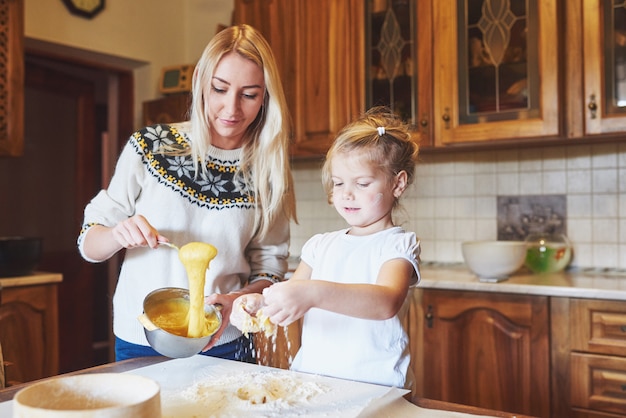 Feliz mamá sonriente en la cocina hornea galletas con su hija.