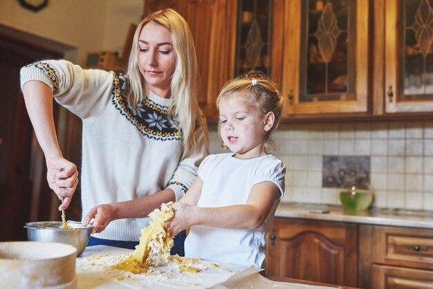 Feliz mamá sonriente en la cocina hornea galletas con su hija.