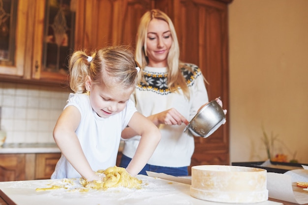 Feliz mamá sonriente en la cocina hornea galletas con su hija.