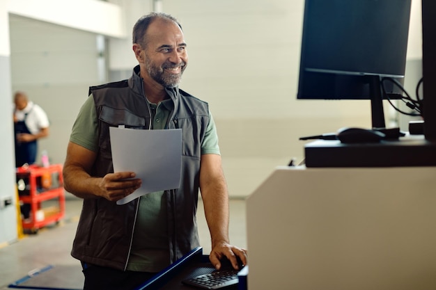 Feliz mecánico adulto medio trabajando en una computadora en un taller de reparación de automóviles