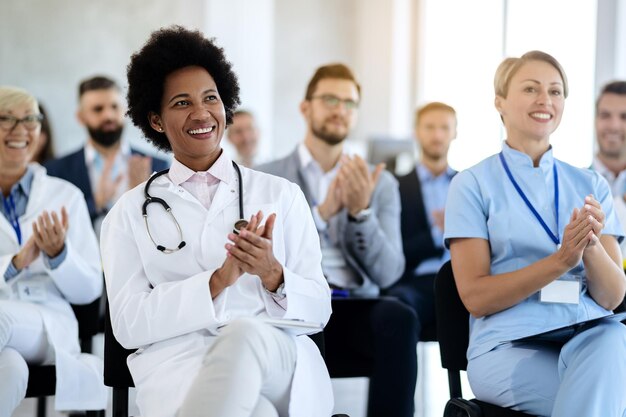 Feliz médico afroamericano aplaudiendo mientras asistía a un seminario de atención médica