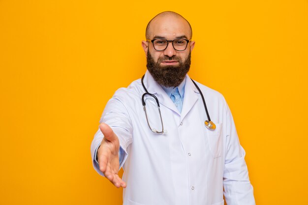 Feliz médico hombre barbudo en bata blanca con estetoscopio alrededor del cuello con gafas mirando sonriendo amable ofreciendo saludo de mano