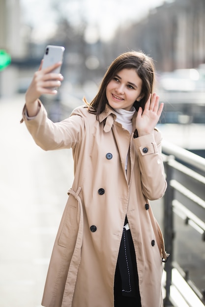 Feliz morena sonriente tiene una videollamada en su teléfono afuera