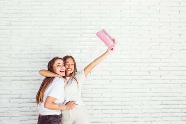 Feliz mujer abrazando a su amiga y levantando sus brazos con un regalo