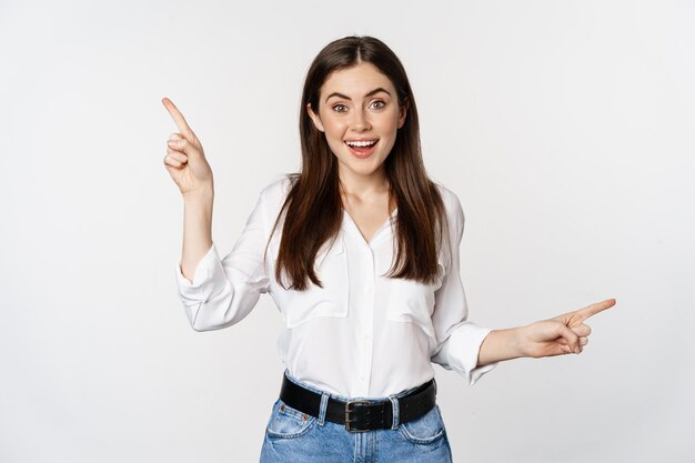 Feliz mujer adulta sonriente apuntando hacia los lados, mostrando dos opciones, productos en venta, logotipo o diagrama, de pie sobre fondo blanco.