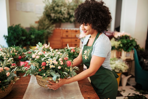 Feliz mujer africana arreglo cesta de flores en el escritorio