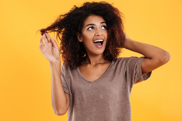 Feliz mujer africana tocando su cabello y mirando hacia arriba