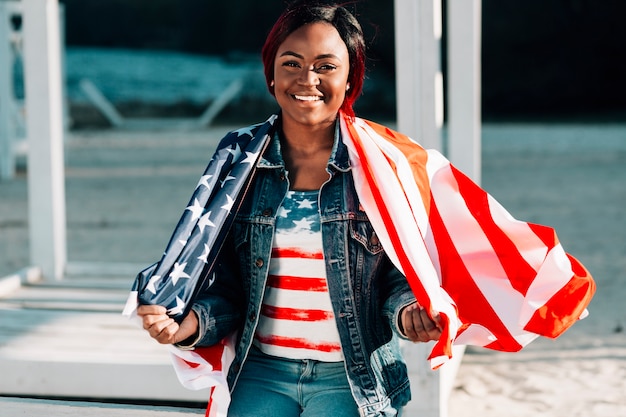 Feliz mujer afroamericana envuelta en la bandera de Estados Unidos