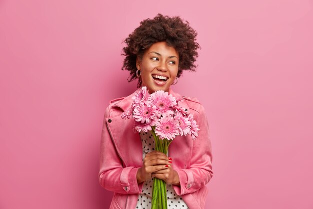 Feliz mujer afroamericana sincera tiene ramo de flores de gerberas, tiene un estado de ánimo festivo positivo,