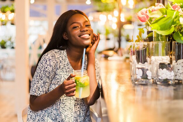 Feliz mujer afroamericana con vaso de limonada natural en café. Bebida detox