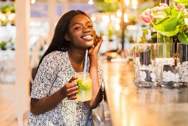 Feliz mujer afroamericana con vaso de limonada natural en café. Bebida detox