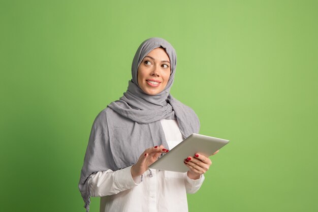 Feliz mujer árabe en hijab con laptop. Retrato de niña sonriente, posando en el estudio verde.