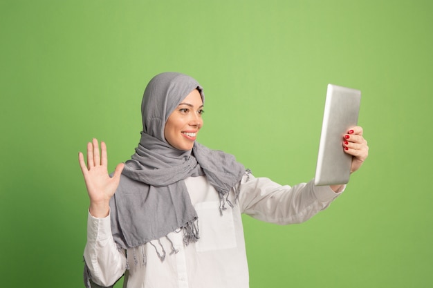 Feliz mujer árabe en hijab con tableta. Retrato de niña sonriente, posando en el fondo verde del estudio.