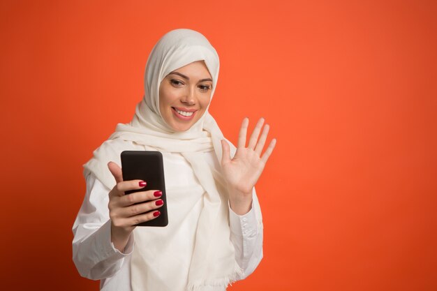 Feliz mujer árabe en hijab con teléfono móvil haciendo selfie.