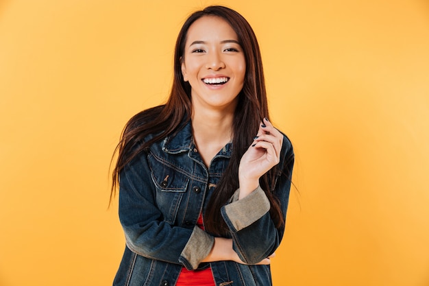 Feliz mujer asiática en chaqueta vaquera sosteniendo su cabello