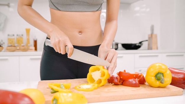 Feliz mujer asiática cortar un montón de pimiento preparar ingrediente para hacer comida en la cocina