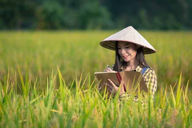 Feliz mujer asiática escribir notas en campos de arroz