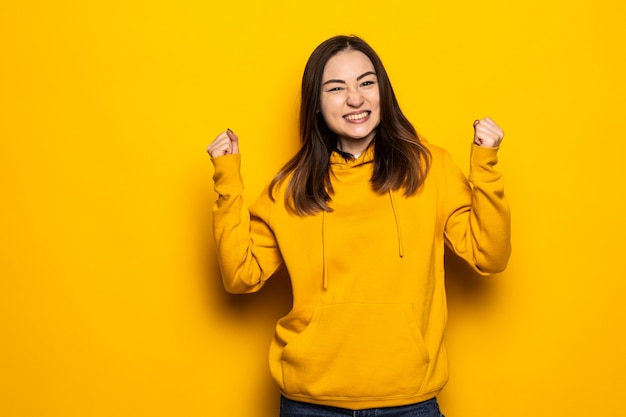 Feliz mujer asiática hacer gesto ganador aislado sobre pared amarilla